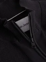 Sweater de punto negro con cuello alto y cierre frontal de cremallera. Presenta un pequeño parche con el logo 'ck' en la manga izquierda.