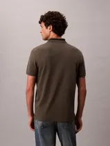 Chomba de piqué color verde militar, de corte regular y manga corta, con cuello clásico y cartera de dos botones. Presenta detalles de líneas en contraste en el cuello y monograma CK bordado en el pecho.
