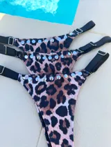 Colaless de bikini con estampado de leopardo, tiras laterales negras ajustables y detalles de tachas metálicas plateadas en el borde superior.