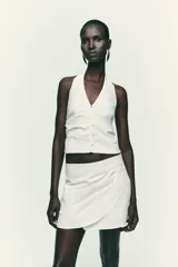 Top negro con cuello halter, escote pico y espalda descubierta. Presenta detalle de frunces laterales y cierre frontal con botones.