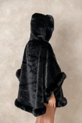 Capa de piel sintética en color negro, con diseño holgado, capucha integrada y bordes con textura de pelo largo.