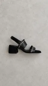 Sandalias de cuero marrón con punta cuadrada, tiras texturizadas con detalles de ojales metálicos y cordones entrelazados, y tira ajustable con velcro en el talón.