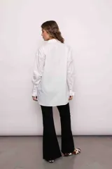 Camisa blanca de algodón con cuello clásico, cierre frontal con botones, mangas largas con puños abotonados y volados en el frente y los puños.