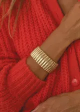 Brazalete ancho color dorado, de diseño rígido y texturado con líneas verticales en relieve.