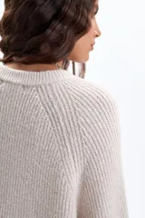 Buzo de tejido de punto en color crudo, con diseño de textura acanalada, cuello redondo, mangas largas holgadas y aberturas laterales en el ruedo.