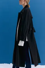 Trench midi de color negro, confeccionado en una mezcla de algodón y nylon con propiedades repelentes al agua. Presenta un diseño holgado con tajos laterales, bolsillos internos y detalle de etiqueta en la espalda.