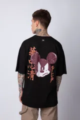 Remera negra de algodón de corte oversize, con mangas cortas y cuello redondo. Estampado pequeño en el frente y diseño grande en la espalda con Mickey Mouse y caracteres orientales en tonos rojizos.