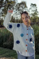 Cardigan de lana color celeste con cuello redondo, cierre frontal con botones color naranja y flores bordadas en azul y celeste.