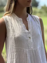 Vestido celeste de lino, sin mangas, con cuello mao y botones de nácar. Presenta varios cortes en su largo, aportando movimiento y un toque moderno a este diseño fresco y elegante.