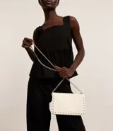 Cartera bandolera pequeña de cuero sintético rojo oscuro, con textura lisa, cierre de hebilla y asa de cadena plateada.