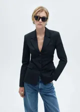 Blazer entallado de color negro con cuello de solapa, cierre frontal de tres botones y bolsillos delanteros con solapa. Presenta un diseño estructurado con detalles fruncidos en los laterales y forro interior.
