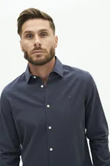 Camisa de manga larga lisa con cuello clásico y cierre frontal de botones. Presenta un ajuste regular y un pequeño logo bordado en el pecho.