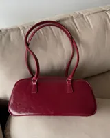 Cartera tipo baguette de cuero sintético color borgoña, con doble asa corta y cierre superior con cremallera.