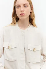 Chaqueta bomber color beige melange, de lino, con cuello mao, cierre frontal con botones a presión, dos bolsillos con solapa en el pecho y puños y cintura elastizados.