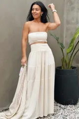 Conjunto de dos piezas color beige confeccionado en algodón de India, compuesto por un top strapless fruncido con detalle de lurex y una falda larga de caída fluida con paneles escalonados.
