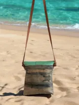 Cartera y bandolera de cuero Emi línea Ottenta, diseñada por Carolina de Cunto con arte pintado a mano. Presenta una solapa semicircular de cuero verde con textura símil serpiente y broche imán, cuerpo principal con estampado artístico multicolor en tonos celestes, marrones y negros, y correa larga marrón fina.