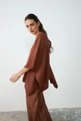 Poncho corto de tejido de punto color habano con sutiles destellos brillantes, de cuello bote y mangas amplias.