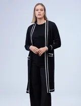 Cardigan largo de punto marca Via Milano, color negro con detalles de rayas blancas en contraste. Presenta un diseño abierto sin botones, bolsillos frontales aplicados y ribetes blancos en la apertura, puños y bolsillos.