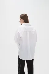 Camisa de algodón blanca de corte holgado, con cuello clásico, cierre frontal parcial con botones y mangas largas con puños anchos.