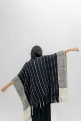 Ruana tejida en tonos azul marino y crudo, con diseño a rayas verticales y detalle de flecos en el ruedo. Presenta un patrón de espiga en los bordes.