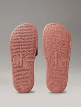 Ojotas tipo slide Calvin Klein Jeans, color rosado, con banda superior de lona de algodón reciclado y logo de la marca estampado en blanco. Presentan suela de EVA con plantilla ergonómica moldeada.