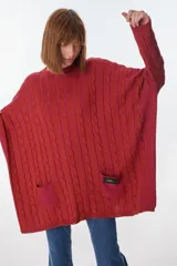 Sweater tipo poncho de punto trenzado color rojo, con cuello redondo, mangas largas y dos bolsillos frontales con el logo "PETRIA".