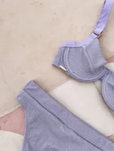 Top de bikini con aros, confeccionado en tela brillante color azul oscuro. Presenta breteles regulables con argollas decorativas y cierre mediante atado en la espalda.