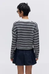 Sweater de punto gris con rayas horizontales en tonos gris oscuro y blanco. Presenta cuello polo blanco y tapeta frontal con cuatro botones marrones. El calce es corto y holgado, con hombros caídos.