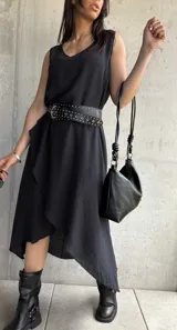 Vestido midi negro sin mangas, con escote redondo y corte asimétrico con volados. Incluye cinturón de cuero con tachas.