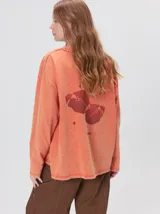 Remera oversize de manga larga color naranja con efecto gastado, cuello redondo y gráfico estampado en la espalda.