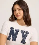 Remera de algodón color crudo, corte new t-shirt ajustado al cuerpo, con cuello redondo y manga corta. Estampa frontal con las letras 'NY' en azul con efecto desgastado.