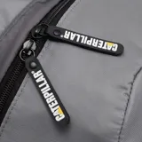 Mochila urbana color gris con detalles en negro, marca Caterpillar. Confeccionada en poliéster 600D con recubrimiento de poliuretano, cuenta con un compartimento principal acolchado para laptop de hasta 15.6 pulgadas, bolsillos laterales de malla y correas ajustables. Incluye elementos reflectantes y el logo de CAT en el frente.