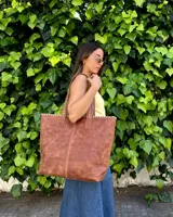 Bolso tipo tote bag color suela, confeccionado artesanalmente en cuero, con costuras visibles decorativas en los bordes y asas de hombro.