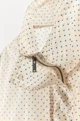 Chaqueta ligera de cuello subido y manga larga con estampado de lunares. Cuenta con bolsillos frontales de vivo, cierre de cremallera y botones a presión ocultos por solapa, y cordones ajustables en el bajo.