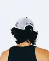 Gorro estilo trucker de color negro con paneles traseros de malla blanca. Presenta bordado frontal con el texto "TWOJEYS" en blanco y dos estrellas contorneadas debajo. El borde de la visera tiene costuras blancas y un acabado desgastado/roto.
