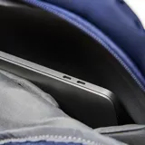 Mochila de diseño minimalista en color azul, confeccionada en material textil. Cuenta con un compartimento principal con cierre de doble cursor, un bolsillo frontal con solapa y cierre de hebilla metálica, y asa superior reforzada.