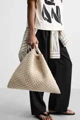 Bolso tipo shopper color crudo, confeccionado en tejido trenzado de algodón con diseño de macramé. Cuenta con dos asas de hombro ajustables que funcionan como cierre del compartimento principal.