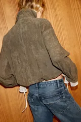 Chaqueta de ante con cuello subido, manga larga y bajo abullonado con elástico. Presenta cierre frontal con cremallera y botones a presión ocultos, además de bolsillos laterales de vivo.