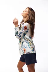 Camisa de manga larga con estampado floral en tonos azules, verdes, naranjas y amarillos sobre fondo blanco.