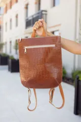 Mochila marrón de cuero con textura tipo piel de cocodrilo, con cierre superior y bolsillo frontal con cierre.