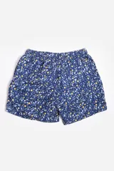 Short de baño celeste con estampado de hojas pequeñas en tonos verdes y blancos. Cuenta con cintura elástica con cordón ajustable, bolsillos laterales y un parche circular con logo en la parte inferior.