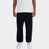Pantalón tipo jogger New Balance de corte holgado, color negro, con cintura elástica y cordón de ajuste interno. Presenta bolsillos laterales y bolsillo posterior con cierre, además de puños elásticos en los tobillos y logo de la marca bordado en la pierna.