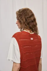 Chaleco de punto color beige, sin mangas, con escote redondo y cierre frontal con botones carey. Presenta diseño calado y silueta amplia.