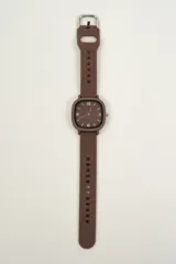 Reloj analógico marrón con caja cuadrada y correa de silicona con hebilla plateada.