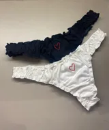 Bombacha tipo less de algodón blanco con bordes fruncidos y un pequeño corazón bordado en hilo rosado en el centro.