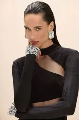 Vestido midi negro de corte ajustado, con mangas largas, cuello alto y aberturas estratégicas con paneles de tul transparente en el pecho y la cintura. Presenta puños decorados con aplicaciones de cristales brillantes.