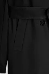 Trench largo de color negro con cuello de solapa, manga larga con trabillas ajustables y cierre frontal cruzado con doble botonadura. Cuenta con bolsillos delanteros de vivo, solapa cortavientos en el pecho y cinturón ajustable del mismo tejido.