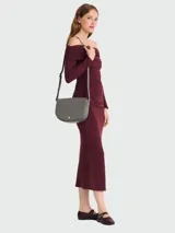 Cartera tipo bandolera de cuero granulado en color gris, con diseño de solapa redondeada y cierre de broche metálico dorado. Incluye correa larga ajustable para llevar al hombro o cruzada.