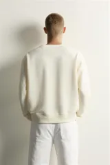 Sudadera de corte relaxed fit en color marfil, con cuello redondo y cierre frontal de botonadura oculta por solapa. Manga larga con acabados en rib y efecto lavado.