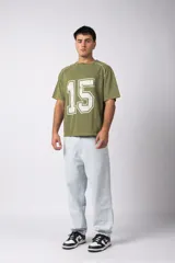 Remera de algodón con estilo deportivo, color verde oliva con efecto de lavado gastado. Presenta el número 15 estampado en blanco en el frente y detalles de costuras con vivos blancos en los hombros. Posee cuello redondo y corte holgado.